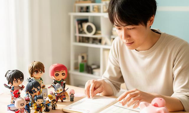 つくば市の明るい部屋で家計ノートと貯金箱を囲み趣味のグッズを整理する若い社会人